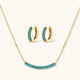 Gold-plated curved necklace and hoop earrings with turquoise cubic zirconia stones on white background.