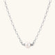 Dainty rhodium-plated silver chain necklace with centered 10mm freshwater pearl and crystal accents on cream background